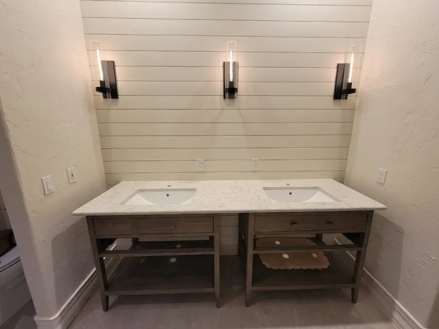 Two wood console vanities with light speckled stone tops and undermount sinks against a shiplap wall