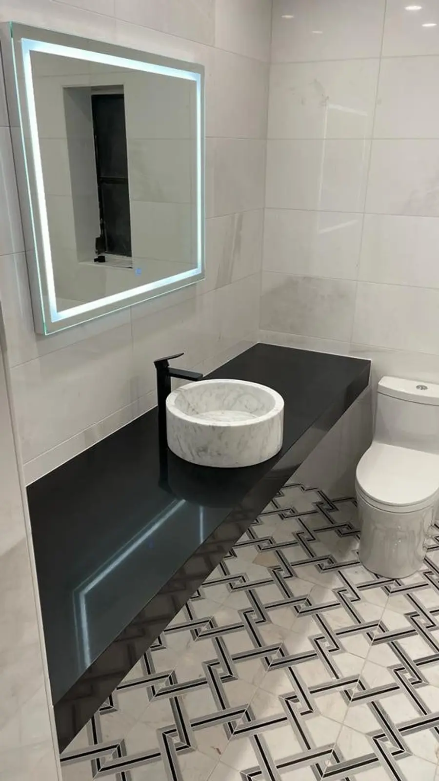 Floating black stone vanity top with a round vessel sink and a lighted mirror in a powder room