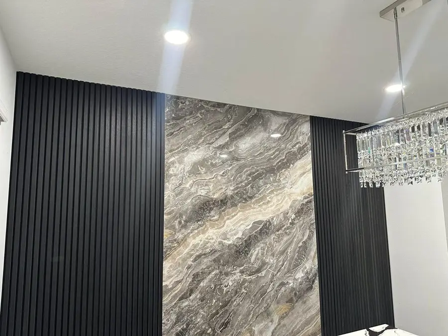 Tall feature wall in gray veined natural stone next to black slatted panels