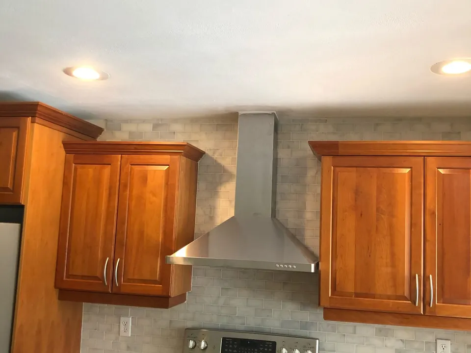 White marble subway tile backsplash behind a range with a stainless hood and wood cabinets