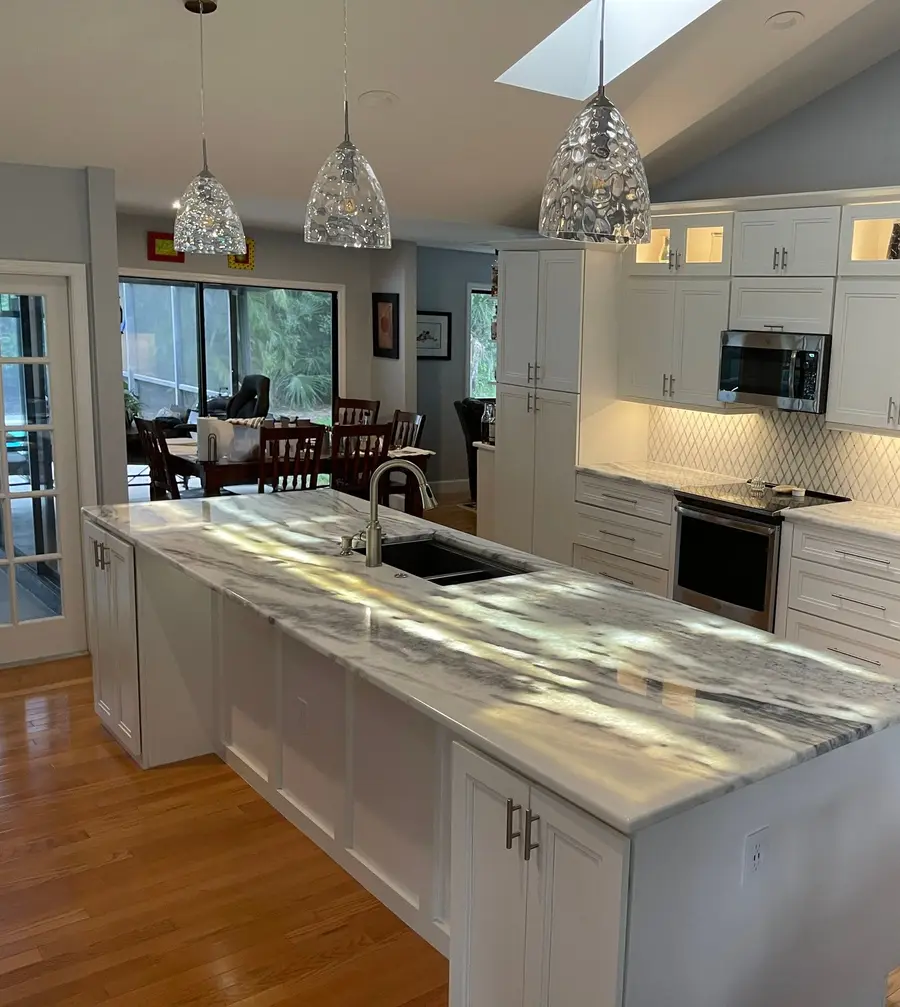 Long kitchen island in Arctic White marble with an undermount sink and white cabinets
