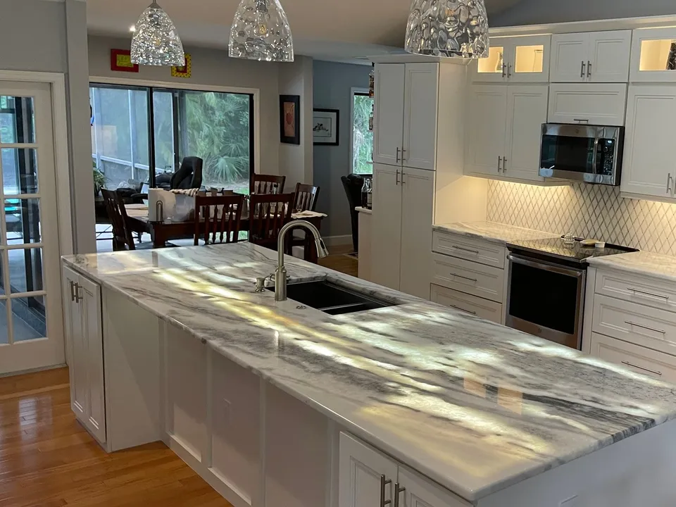 Long kitchen island in Arctic White marble with an undermount sink and white cabinets