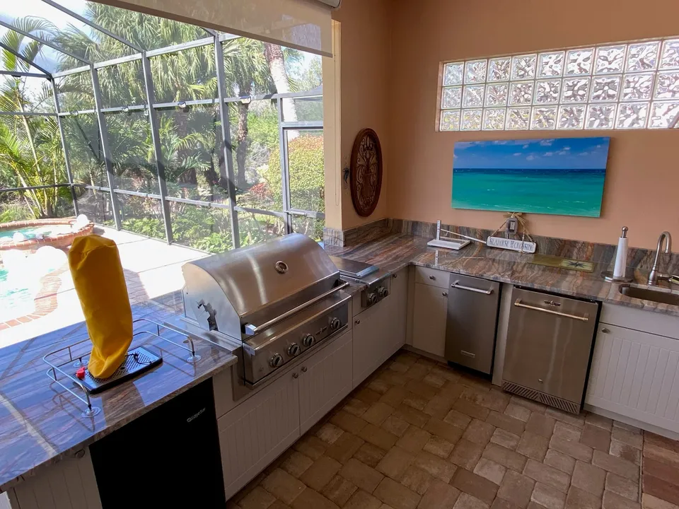 Outdoor kitchen on a screened lanai with veined stone countertops, a built in grill and a bar sink