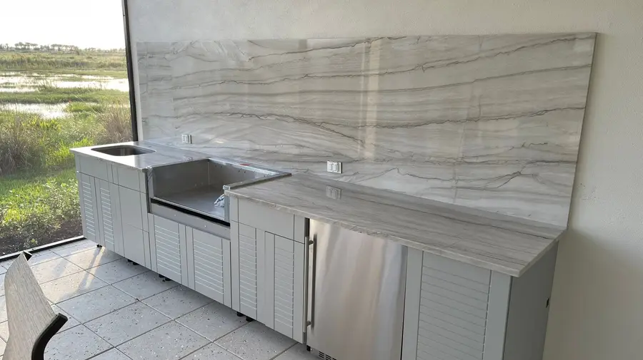 Outdoor kitchen with Mykonos stone countertops and a tall slab backsplash facing a nature preserve
