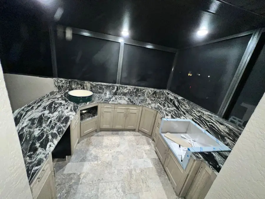 U shaped outdoor kitchen in a screened patio with black and white veined stone countertops