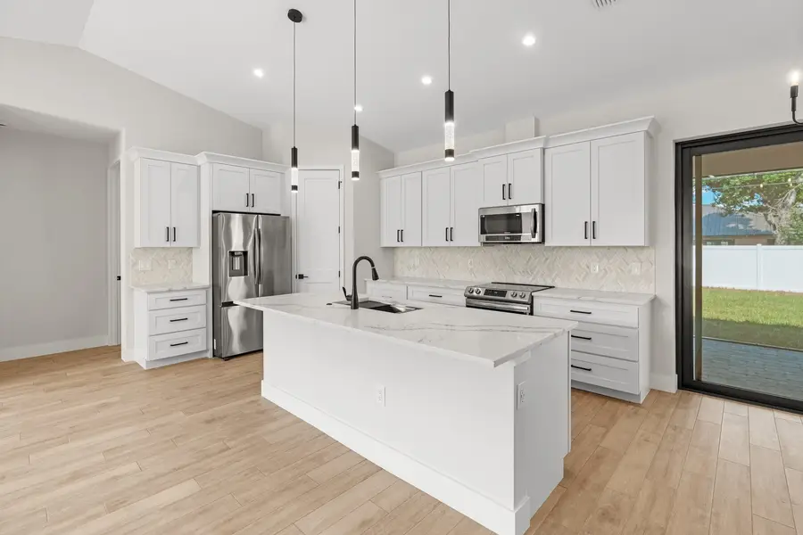 White shaker kitchen with a large island topped in white veined Calacatta quartz and black pendant lights