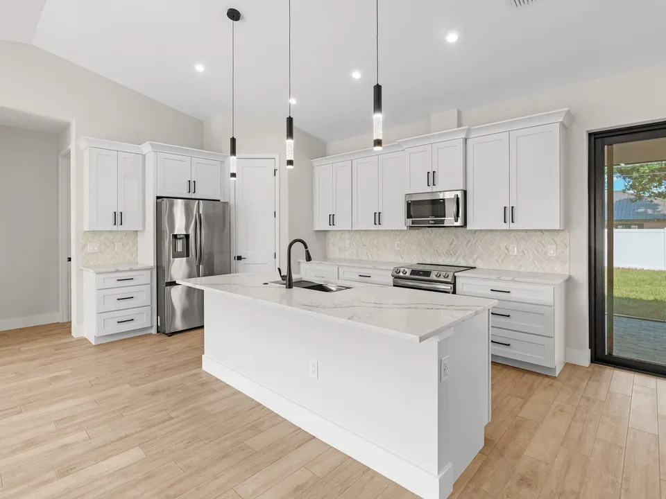 White shaker kitchen with a large island topped in white veined Calacatta quartz and black pendant lights