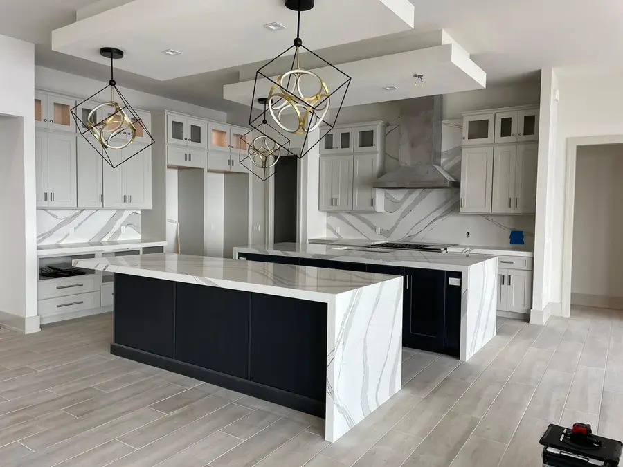 Kitchen with two black islands topped in white veined quartz with waterfall sides and a full height backsplash