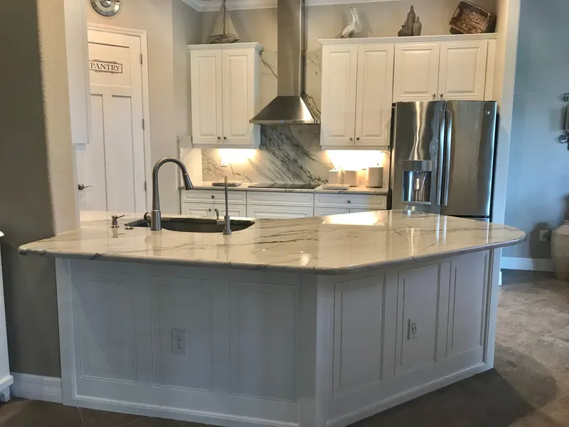 Angled kitchen island in Infinity White quartzite with a stone backsplash behind the range hood